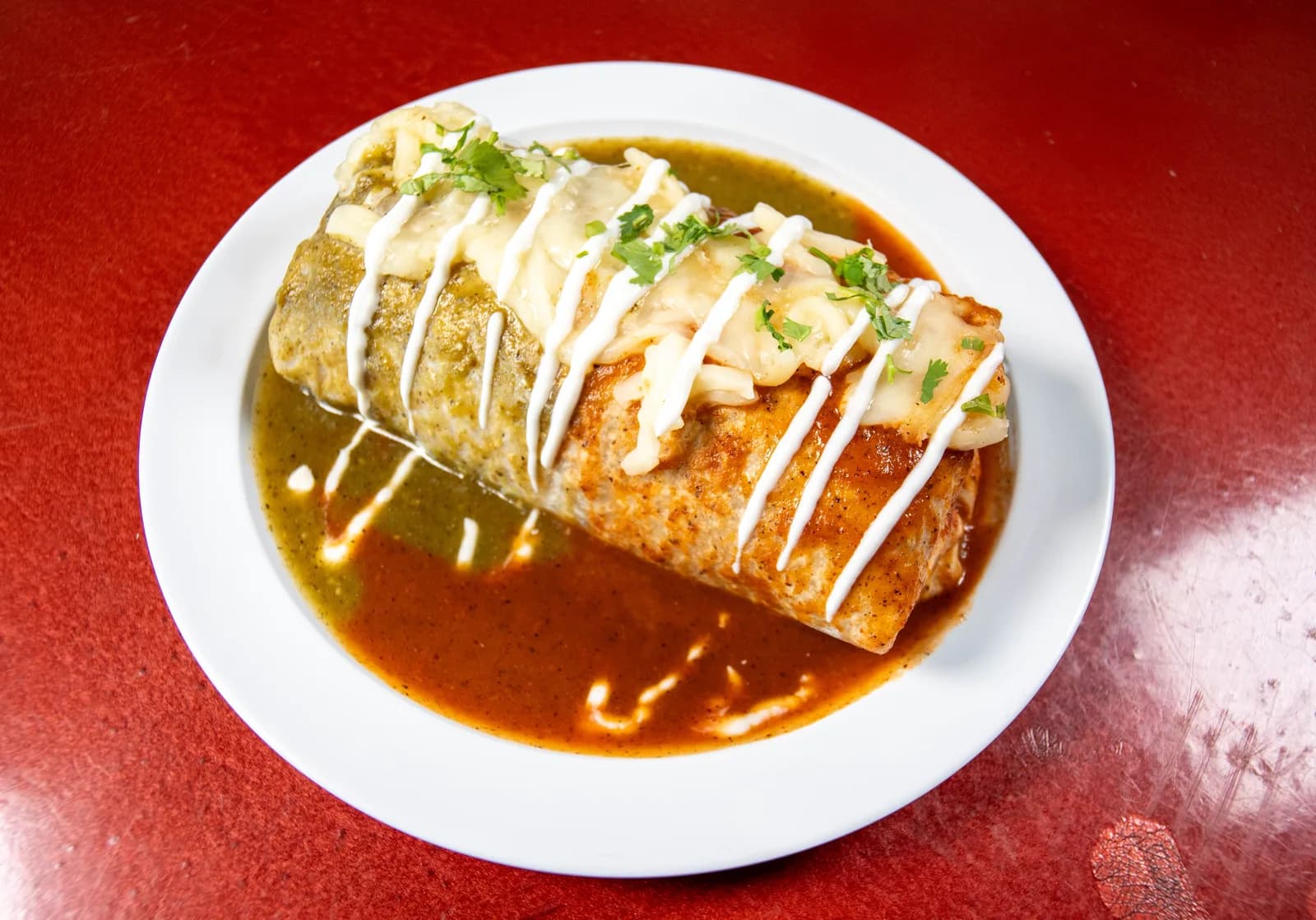 Wet burrito covered in green and red sauce with melted cheese